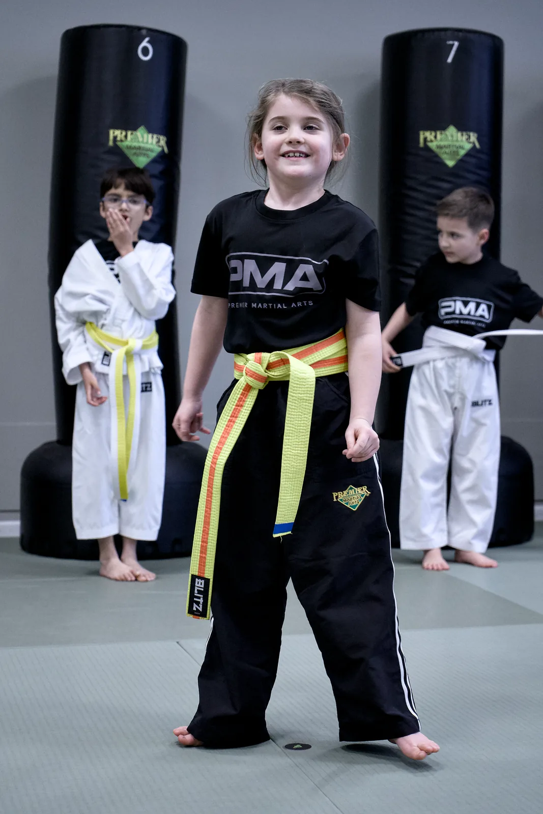 A small child in a yellow belt grinning at the front of the class