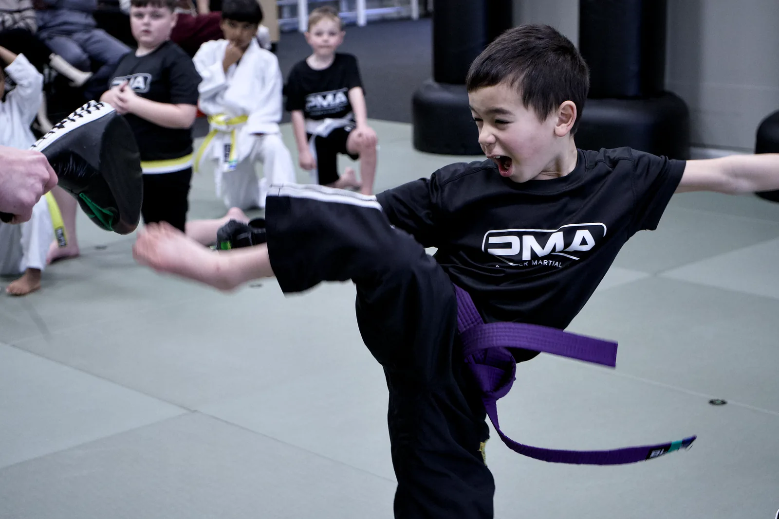 A boy in a purple-striped belt throwing a kick with his full weight behind it