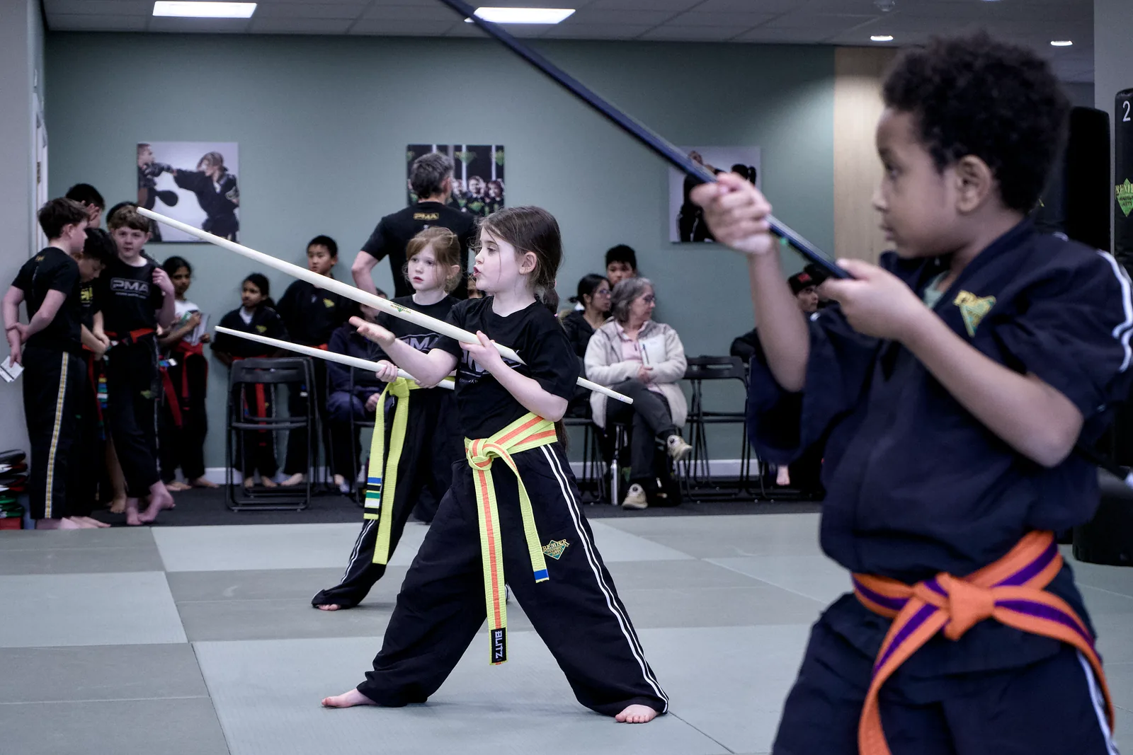 A group of children holding training staffs raised, mid-drill