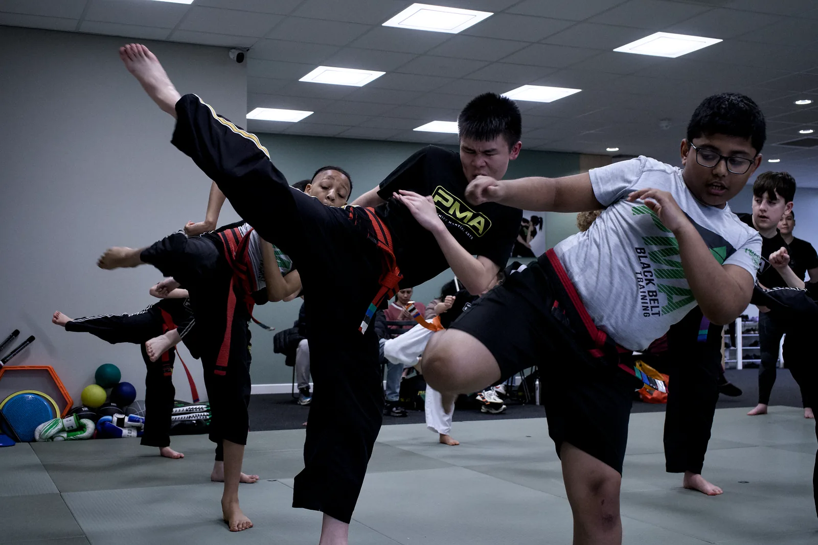 A teenager mid-air in a jumping kick, the class watching from the side