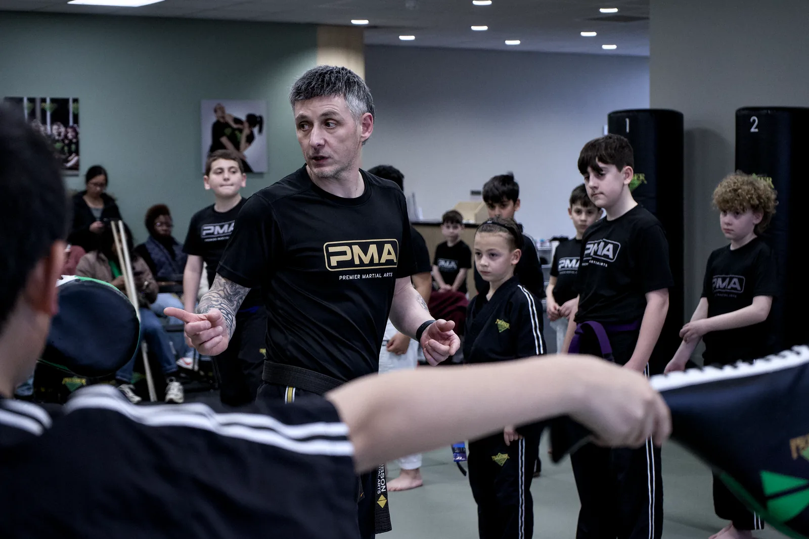 An instructor watching a line of children practise, pads in hand