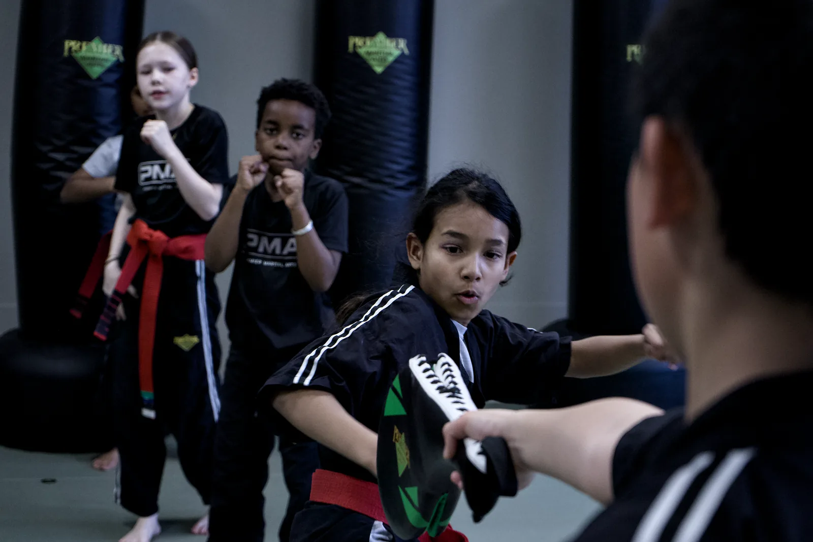 A girl in a red belt throwing a punch at a pad held by her partner