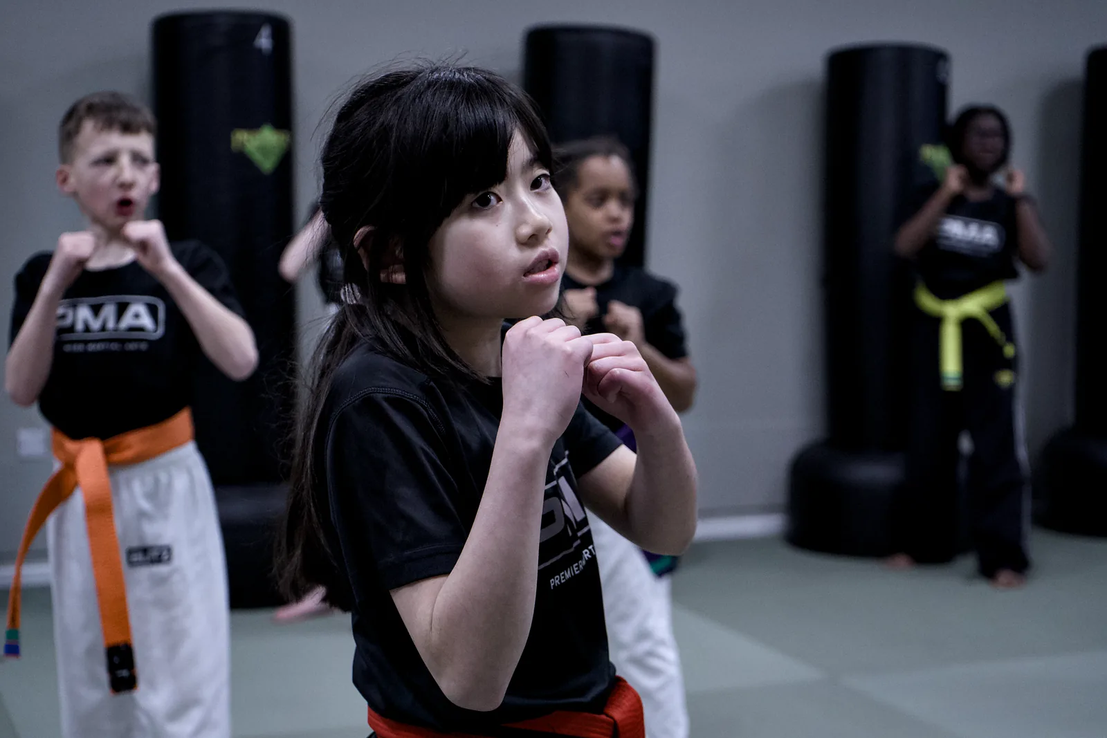 A girl in an orange belt holding a guard, focused on her partner