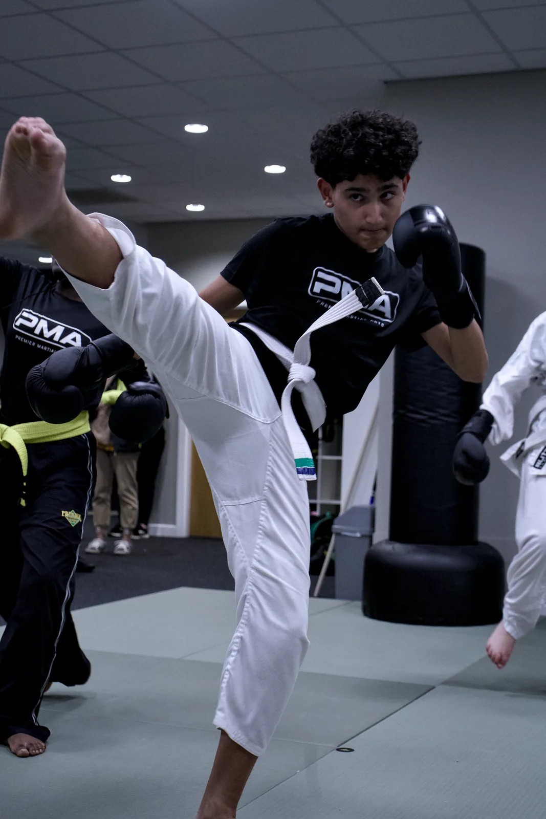 A teenager landing a high taekwondo kick on a pad held at head height