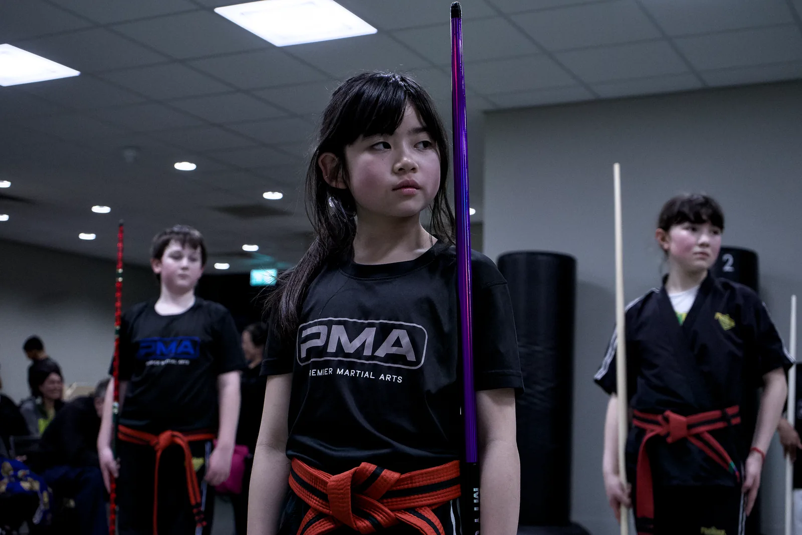 A girl holding a training staff upright while the class works behind her