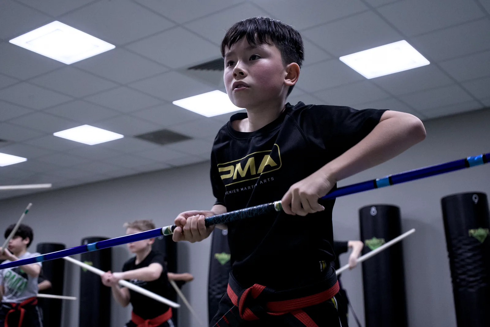 A boy in a red belt swinging a padded training stick in a drill