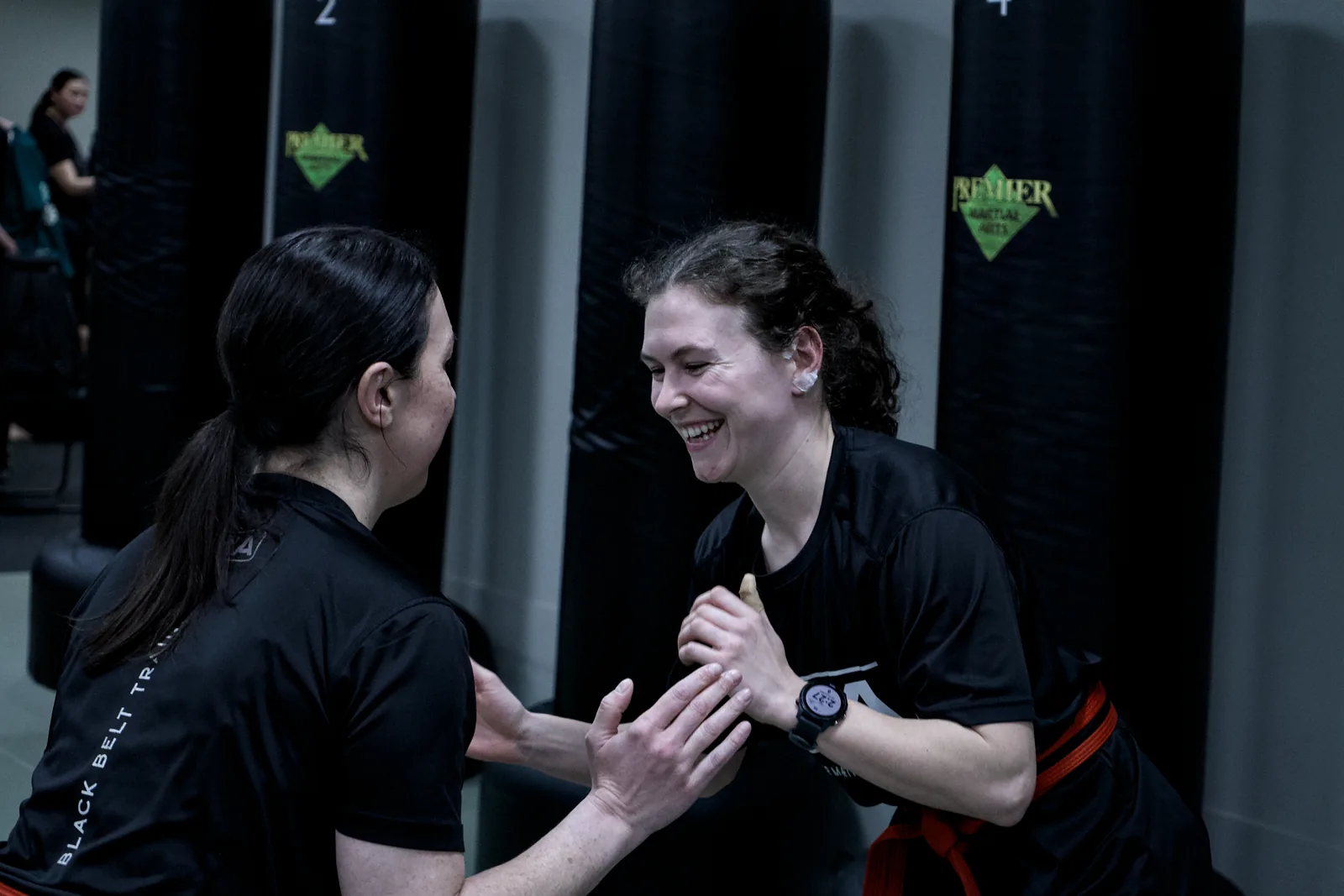 An instructor talking an adult student through a wrist release, both smiling