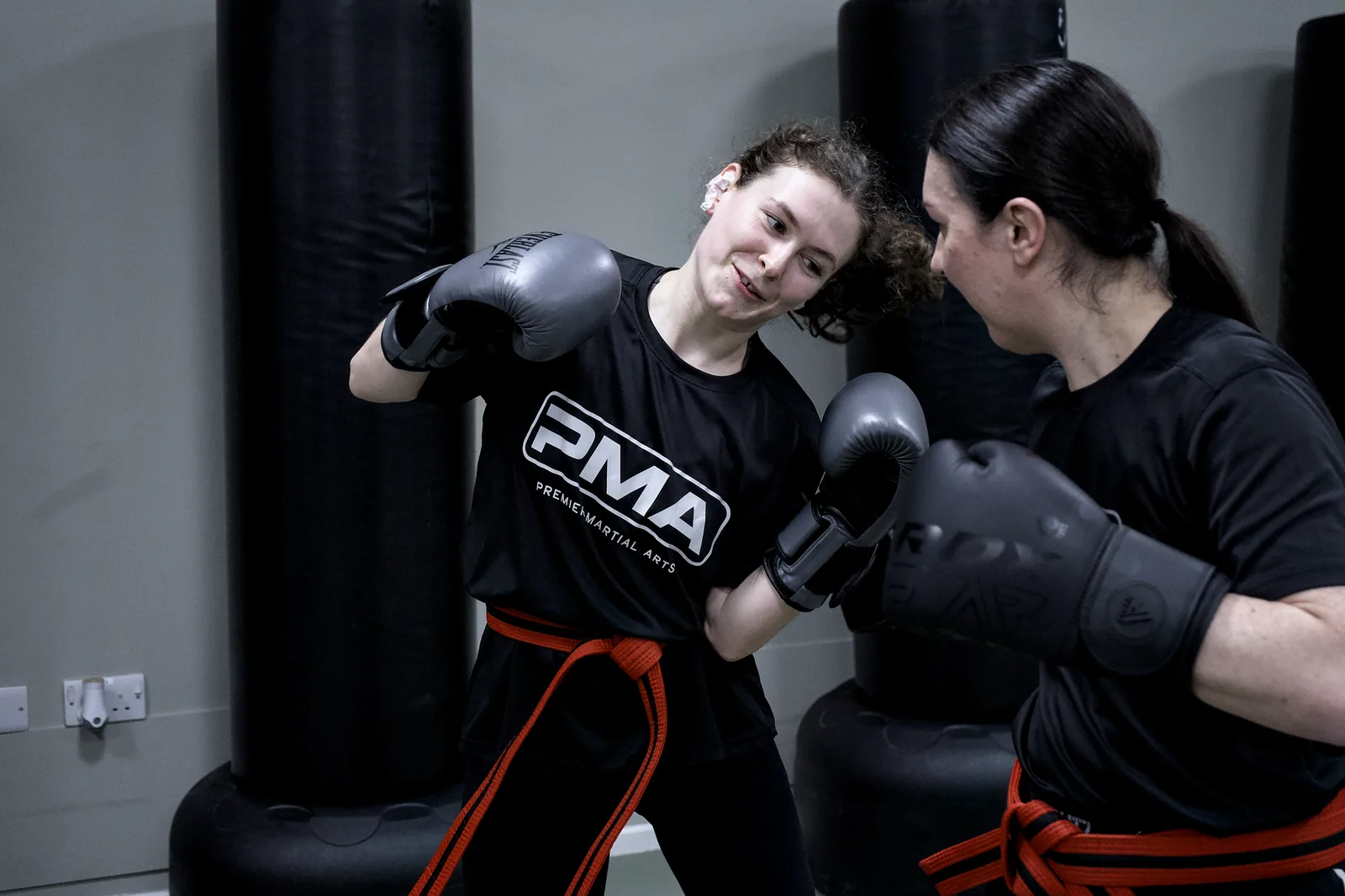 Two adults drilling a jab on the pads, one in a PMA shirt and an orange belt