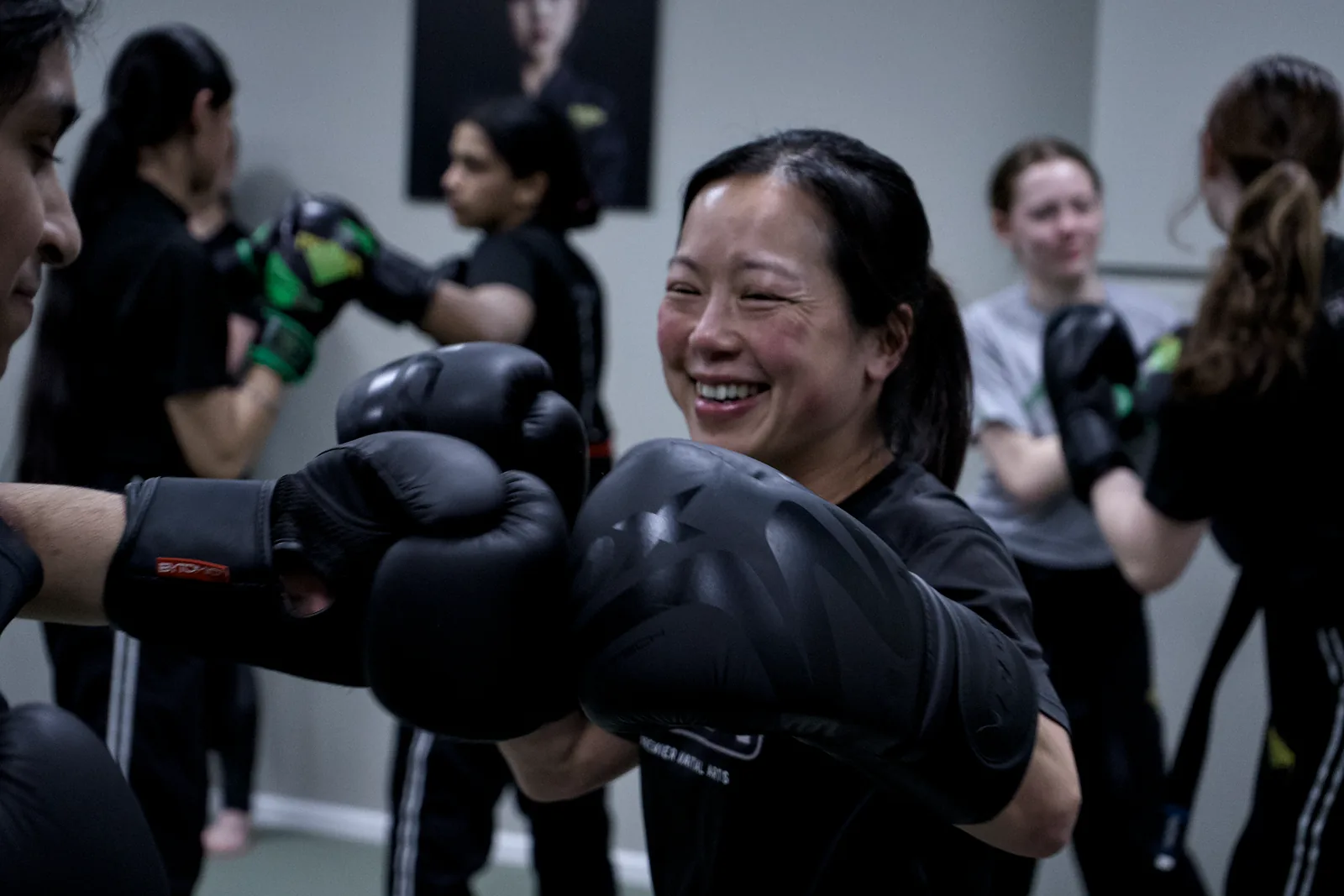 An adult student laughing while working combinations in boxing gloves