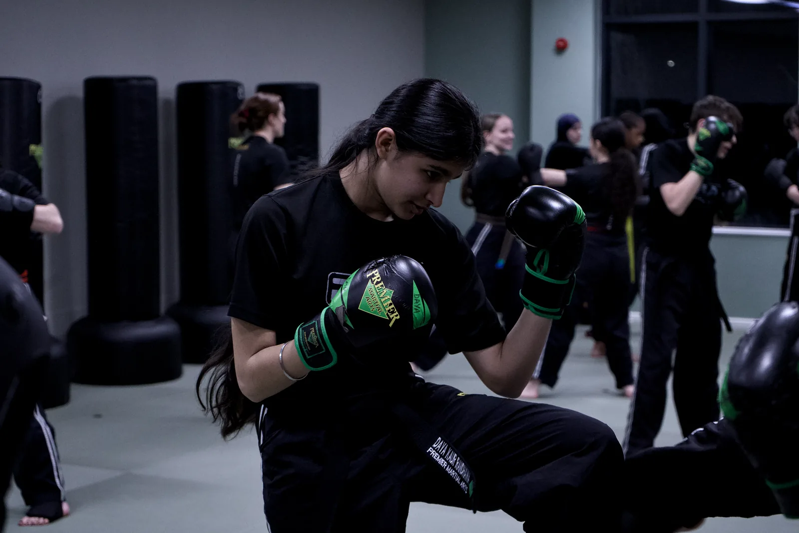 An adult student throwing a knee in green gloves, class behind